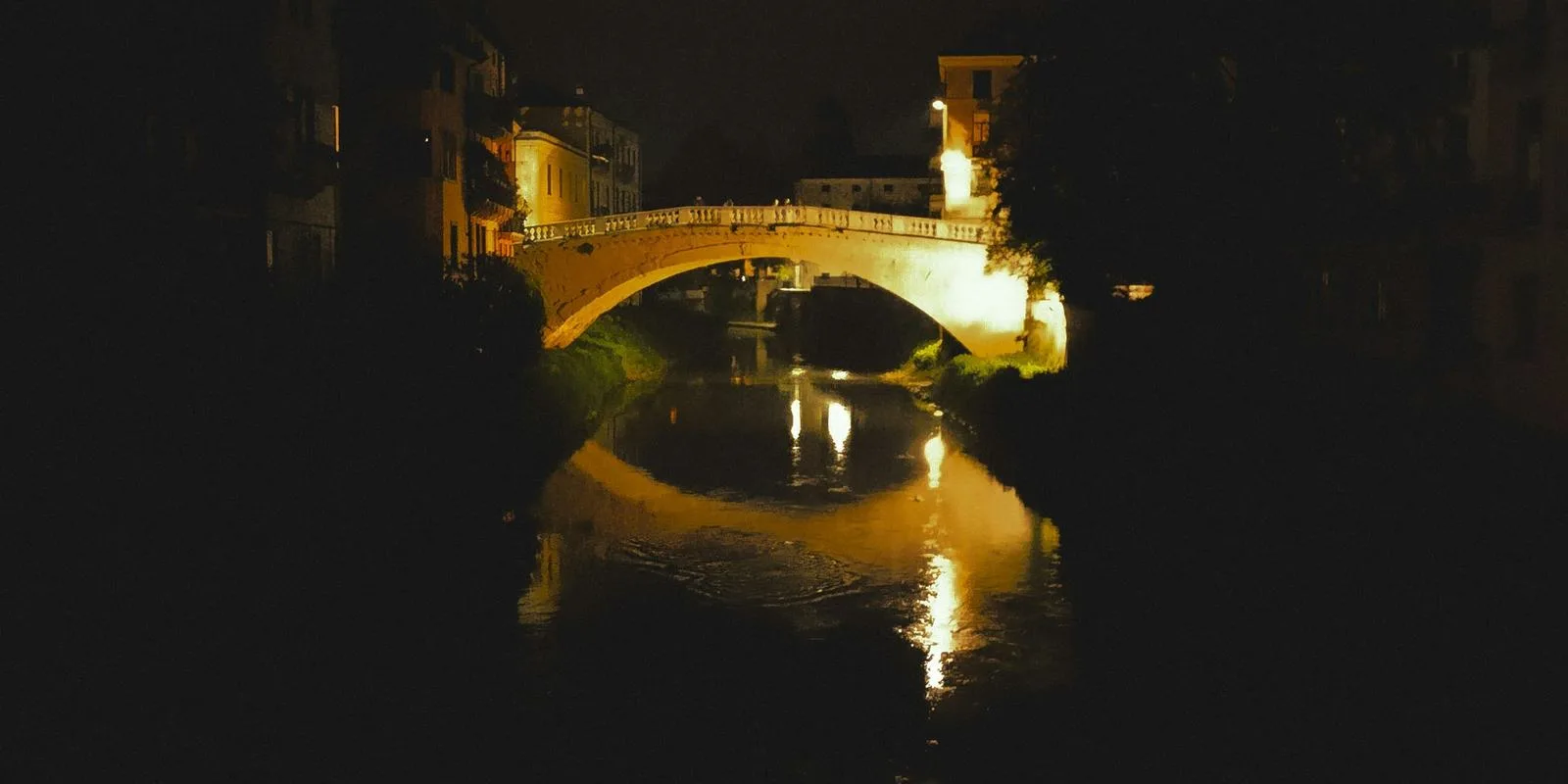 Ponte San Michele lit over the Retrone at night, seen from a window box of flowers