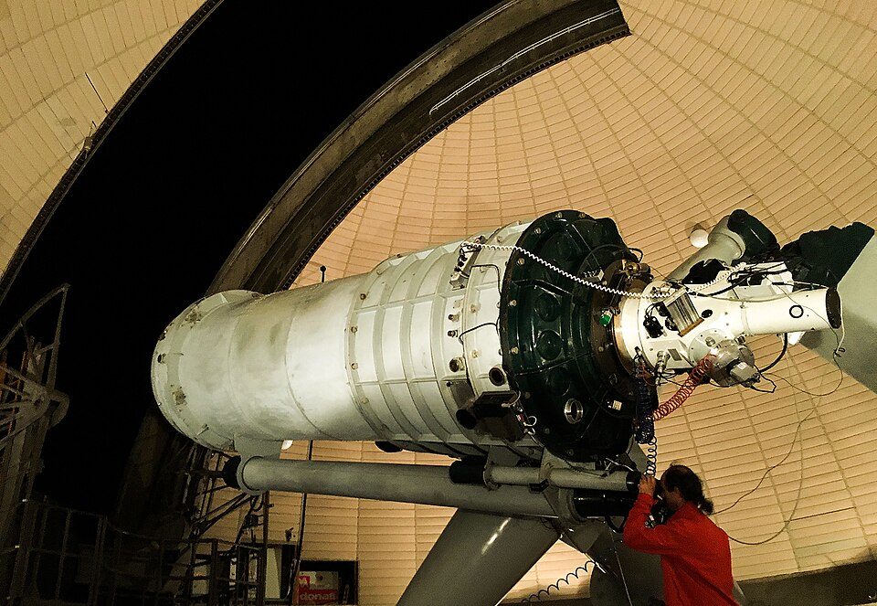 A large telescope inside the observatory dome, with a visitor at the eyepiece